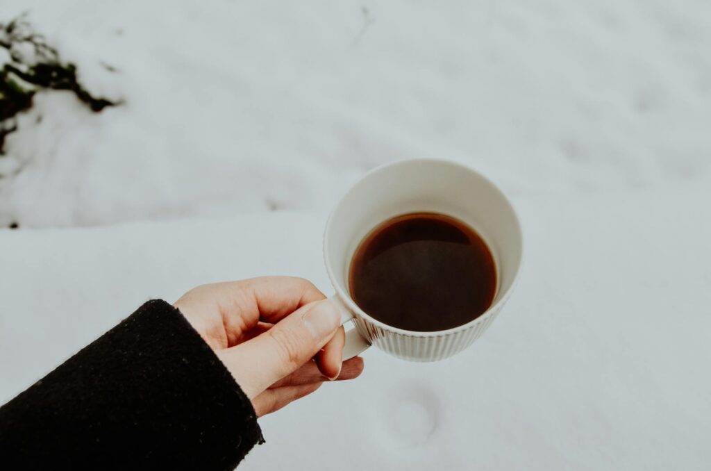 A hand holding a warm cup of coffee against a snowy winter background. for devotional Being Content in Life