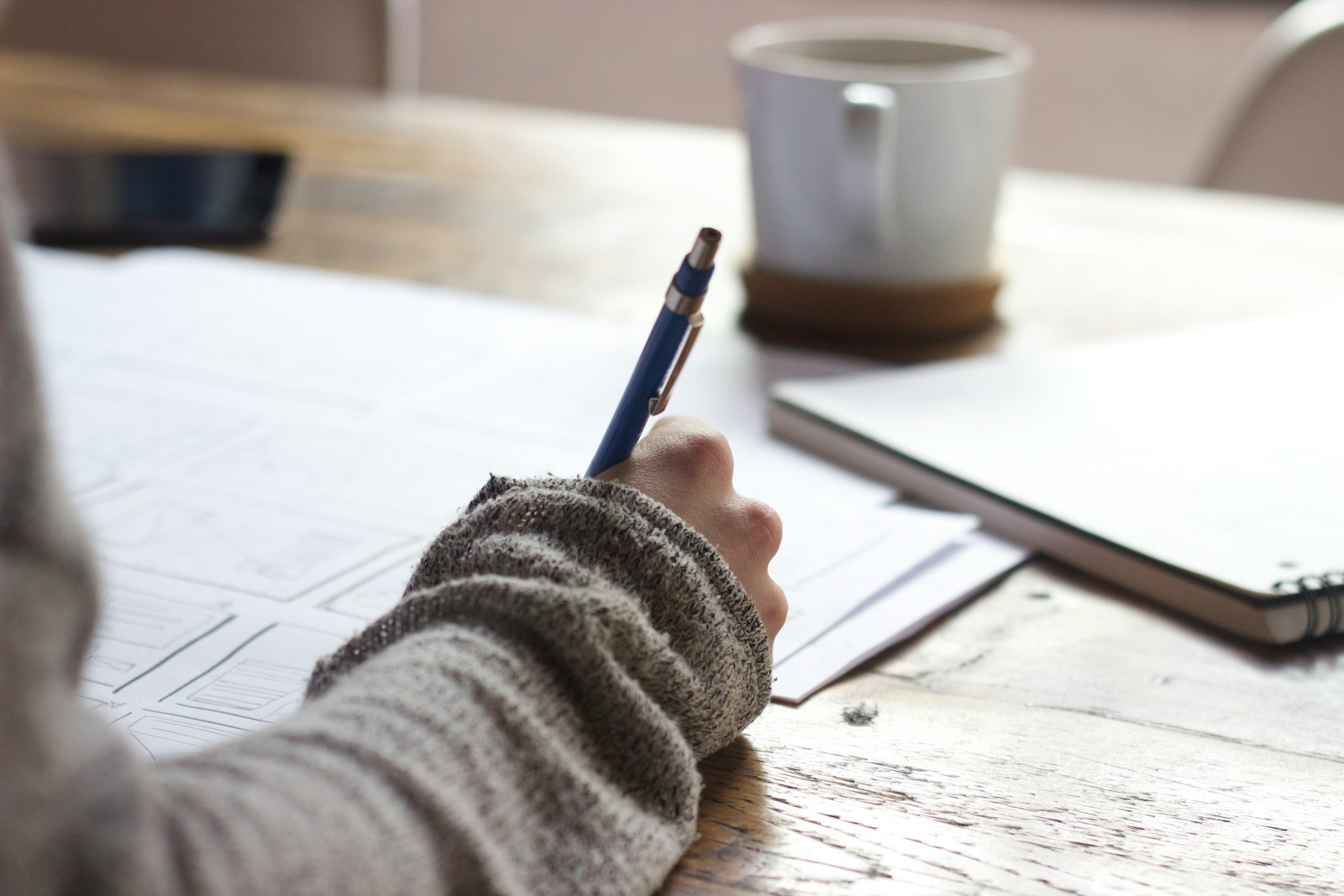 person writing on brown wooden table near white ceramic mug for blog post Distracted Hearts