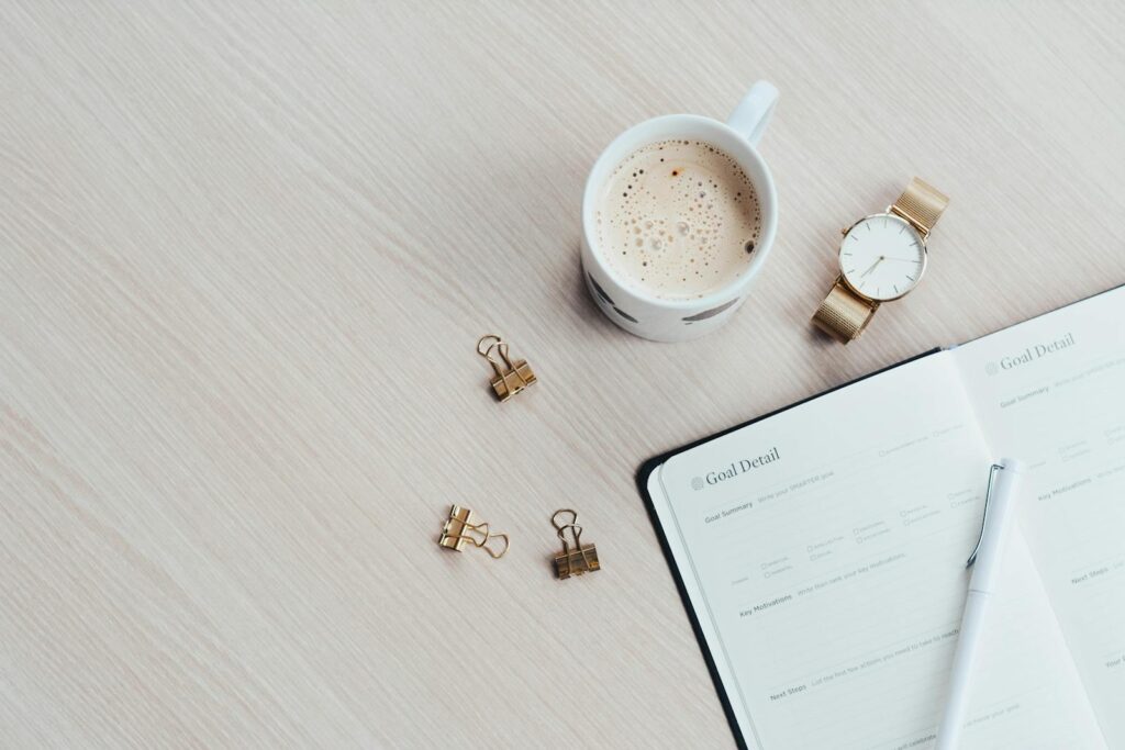 A minimalist desk arrangement featuring a coffee cup, notebook, pen, and wristwatch. for devotional Makings Plans